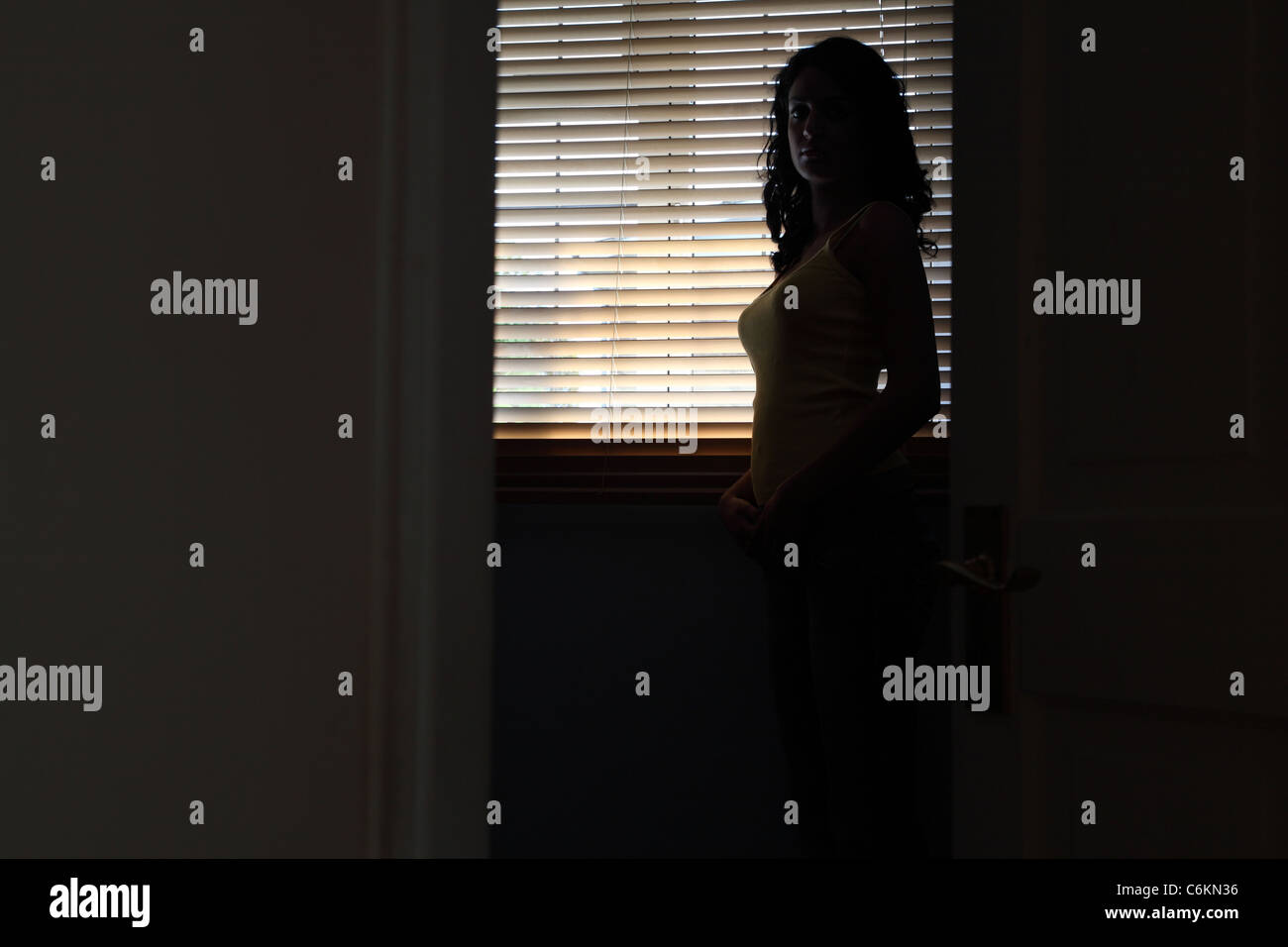 Silhouette of a young woman standing in a dark room the light from a ...