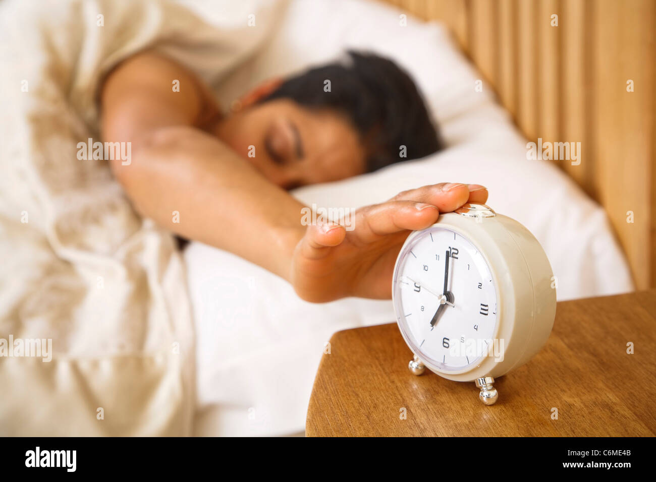 An Indian Asian woman wakes up and reaches to turn off a traditional alarm clock Stock Photo
