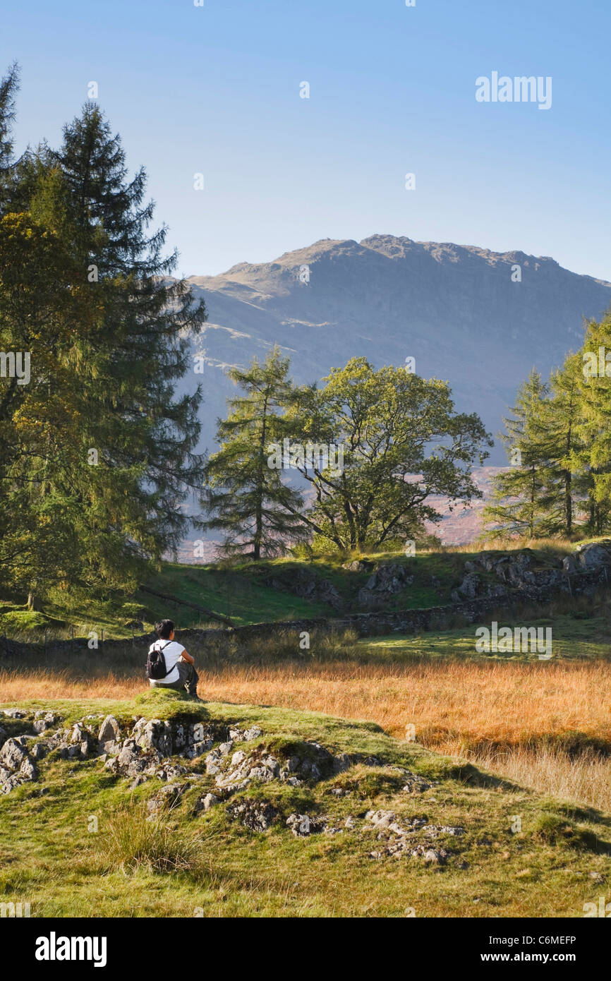 An Asian woman sits and enjoys the view on a hike in the Lake District, UK Stock Photo