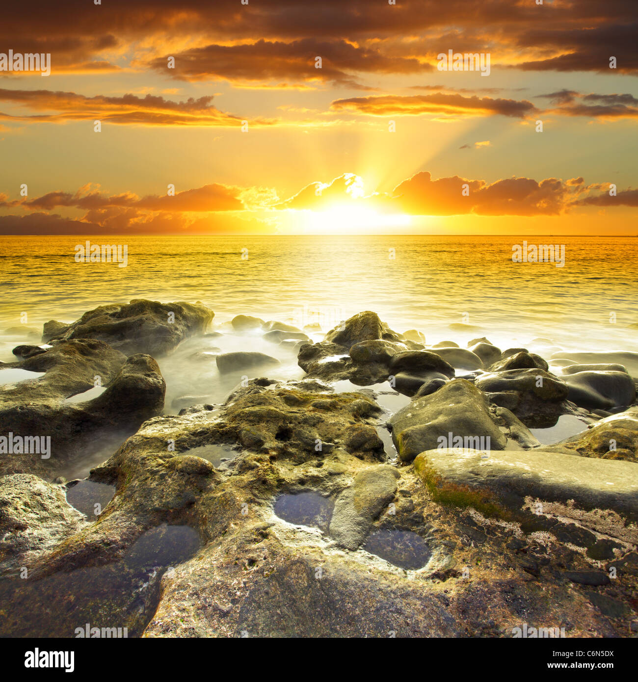 Beautiful orange sundown at rocky beach. Water in motion blur Stock