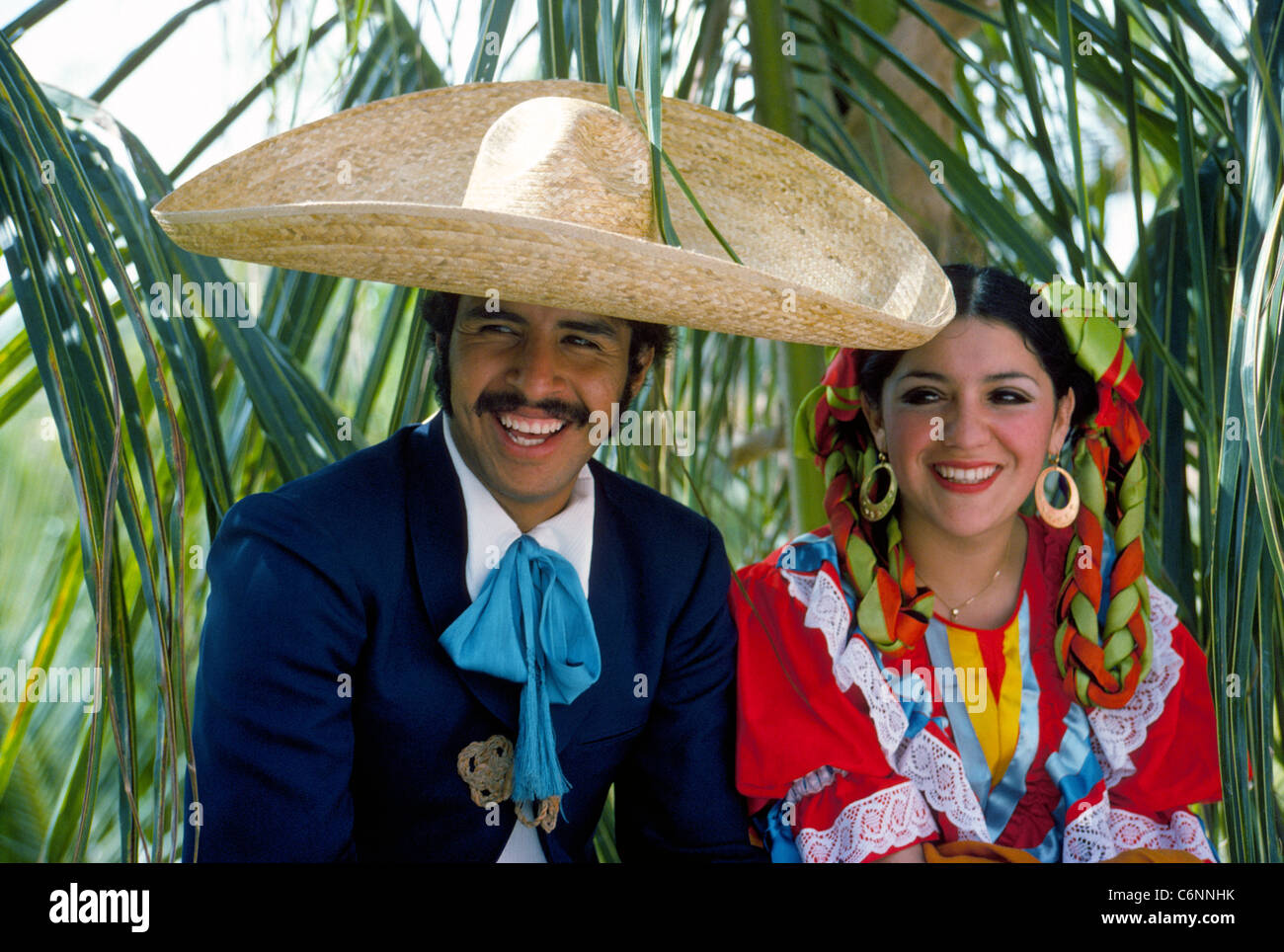 A traditional Mexican folkloric dance couple in their colorful costumes relax in the shade of palms between performances in Puerto Vallarta, Mexico. Stock Photo