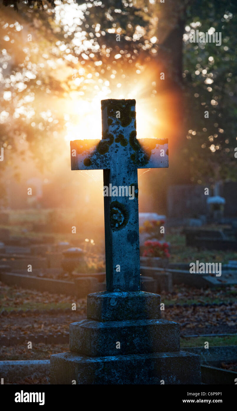 Cemetery Cross headstones lit up in the early morning sunlight through mist. Kings Sutton, Northamptonshire, England Stock Photo