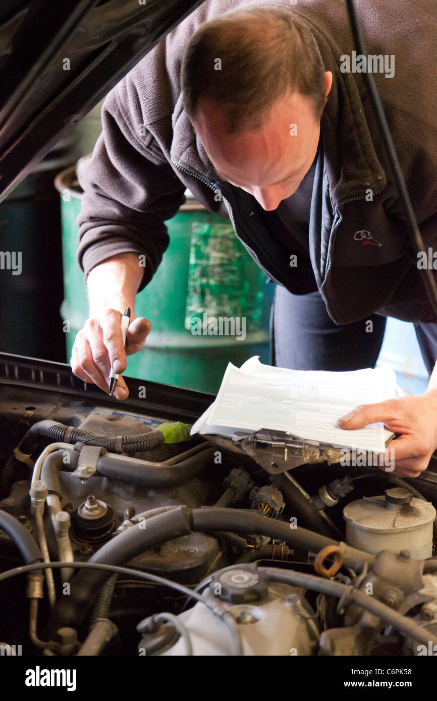 garage mechanic checking underside of a car during an MOT test in the ...
