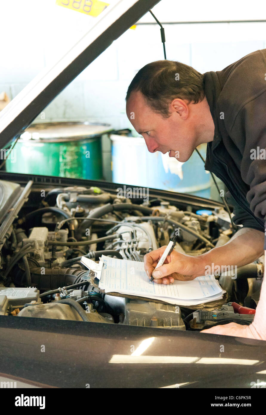garage mechanic checking underside of a car during an MOT test in the ...