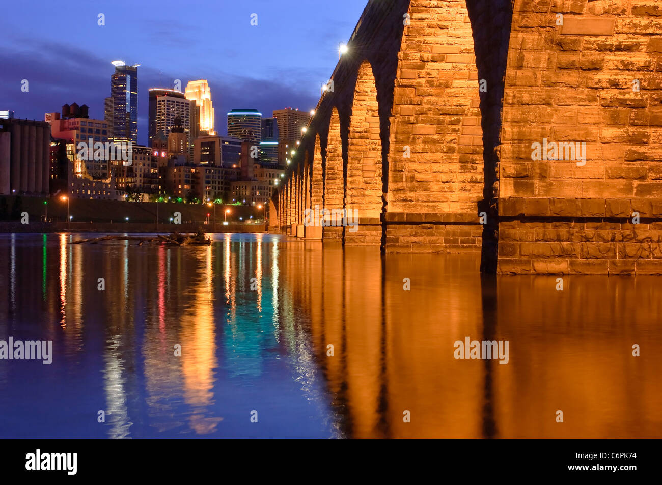 Minneapolis skyline and stone arch bridge at dusk with Mississippi River in foreground. Stock Photo