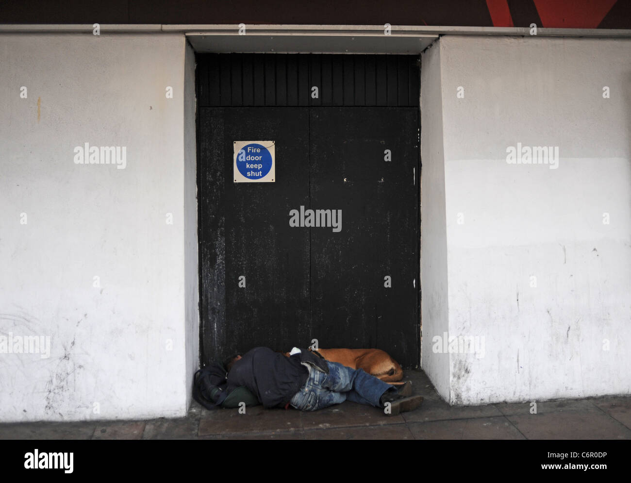 Sleeping Rough or Rough sleepers city centre Brighton - Man and his dog slumped asleep in a doorway in West Street Brighton UK Stock Photo