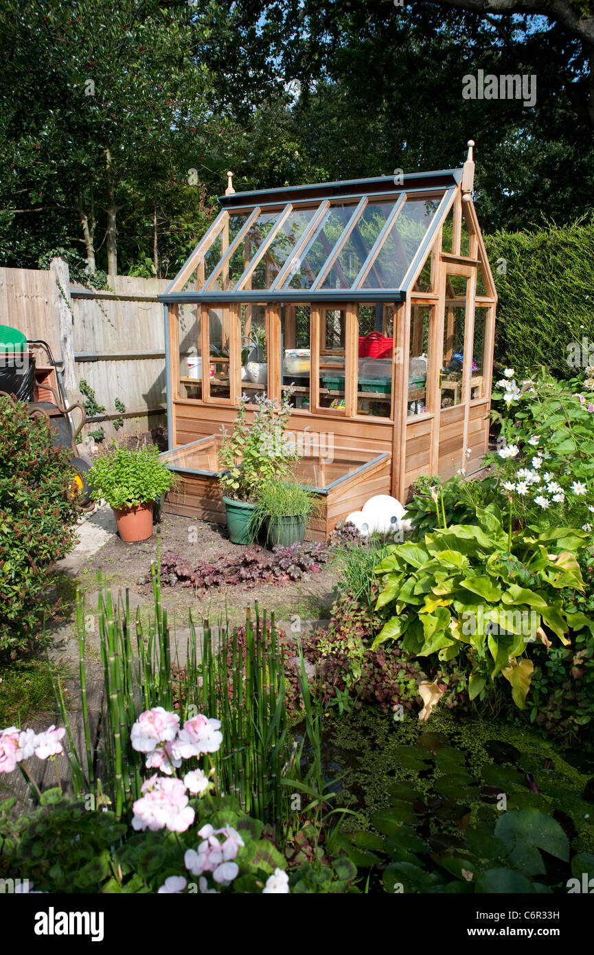 Brand new cute small greenhouse in a private Garden in London with lots of bedding plants in front and some trees. Stock Photo