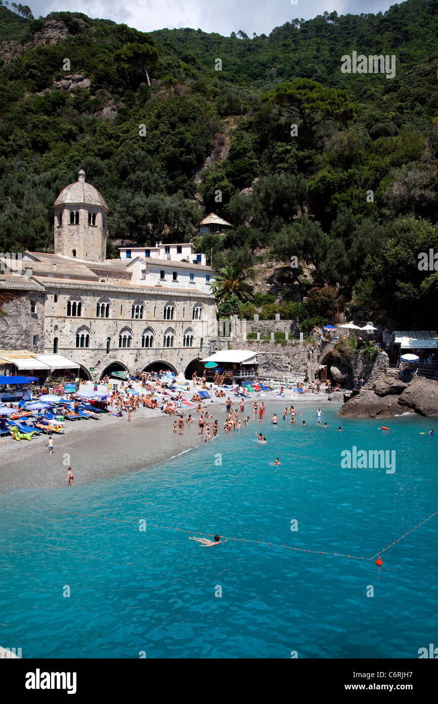 View of San Fruttuoso di Camogli, Liguria, Italy, with medieval abbey, old buildings, blue sea, rocky beach and people swimming Stock Photo