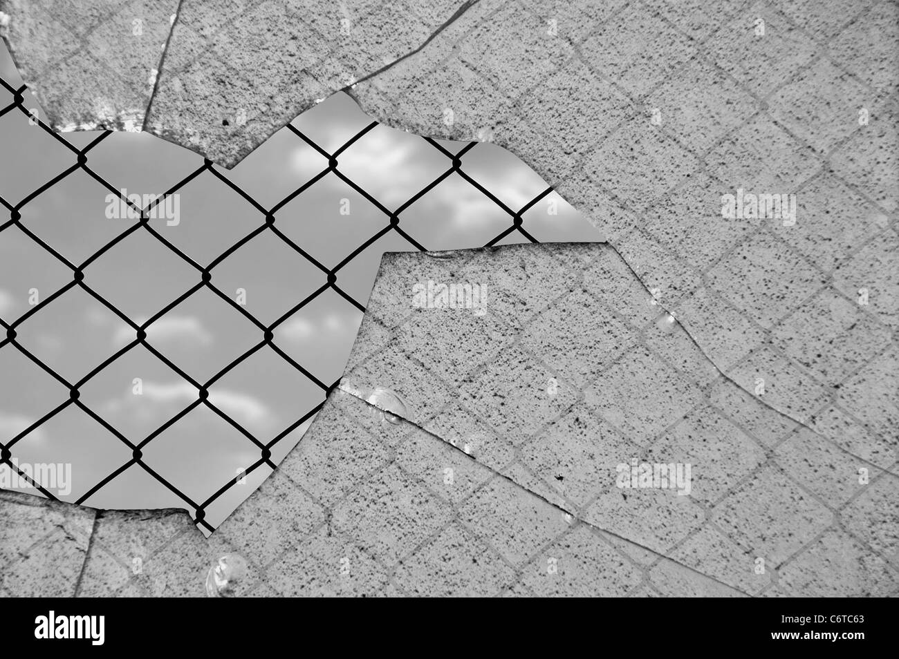 Broken glass and chain link wired fence against the sky. Black and white. Stock Photo