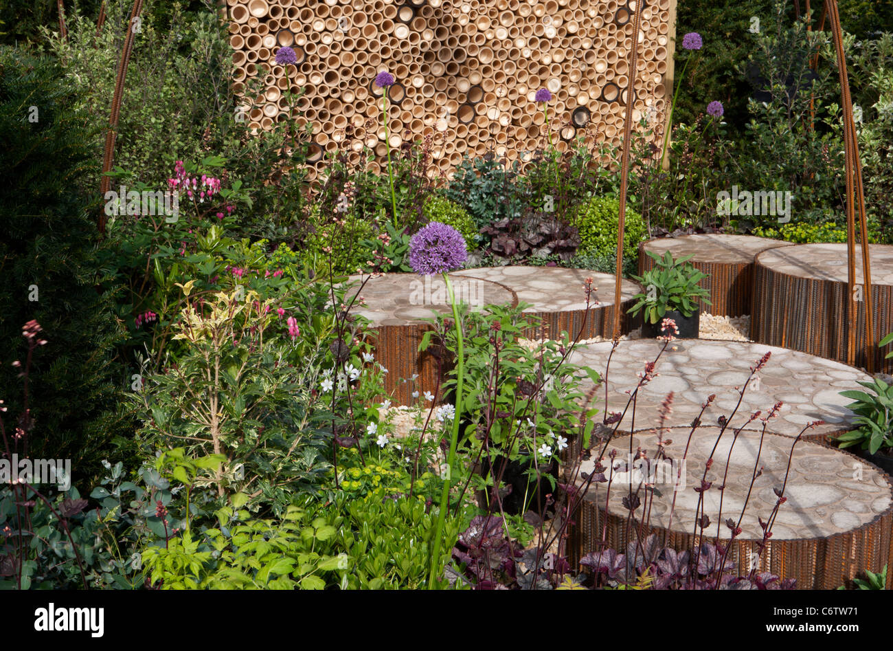 A wildlife friendly garden with circular circle raised patio area stone paving paved and insect hotel motel wall fence UK Stock Photo