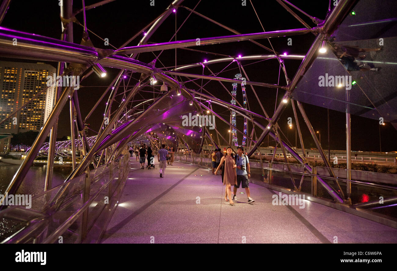 People walking along the modern Helix bridge with the Singapore flyer  in the background, the Marina, Singapore Asia Stock Photo