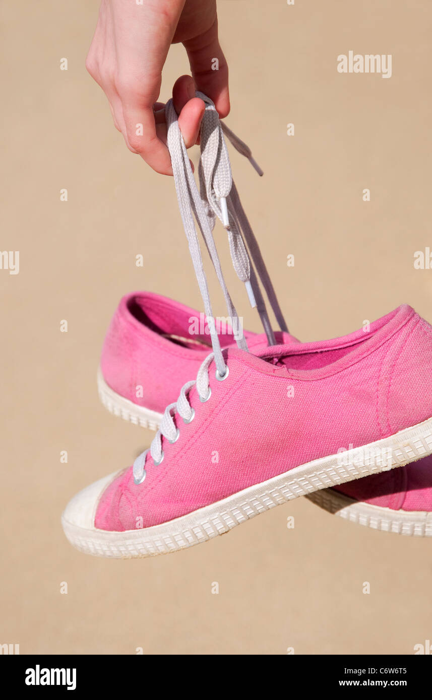 female hand carrying pink plimsolls on beach Stock Photo