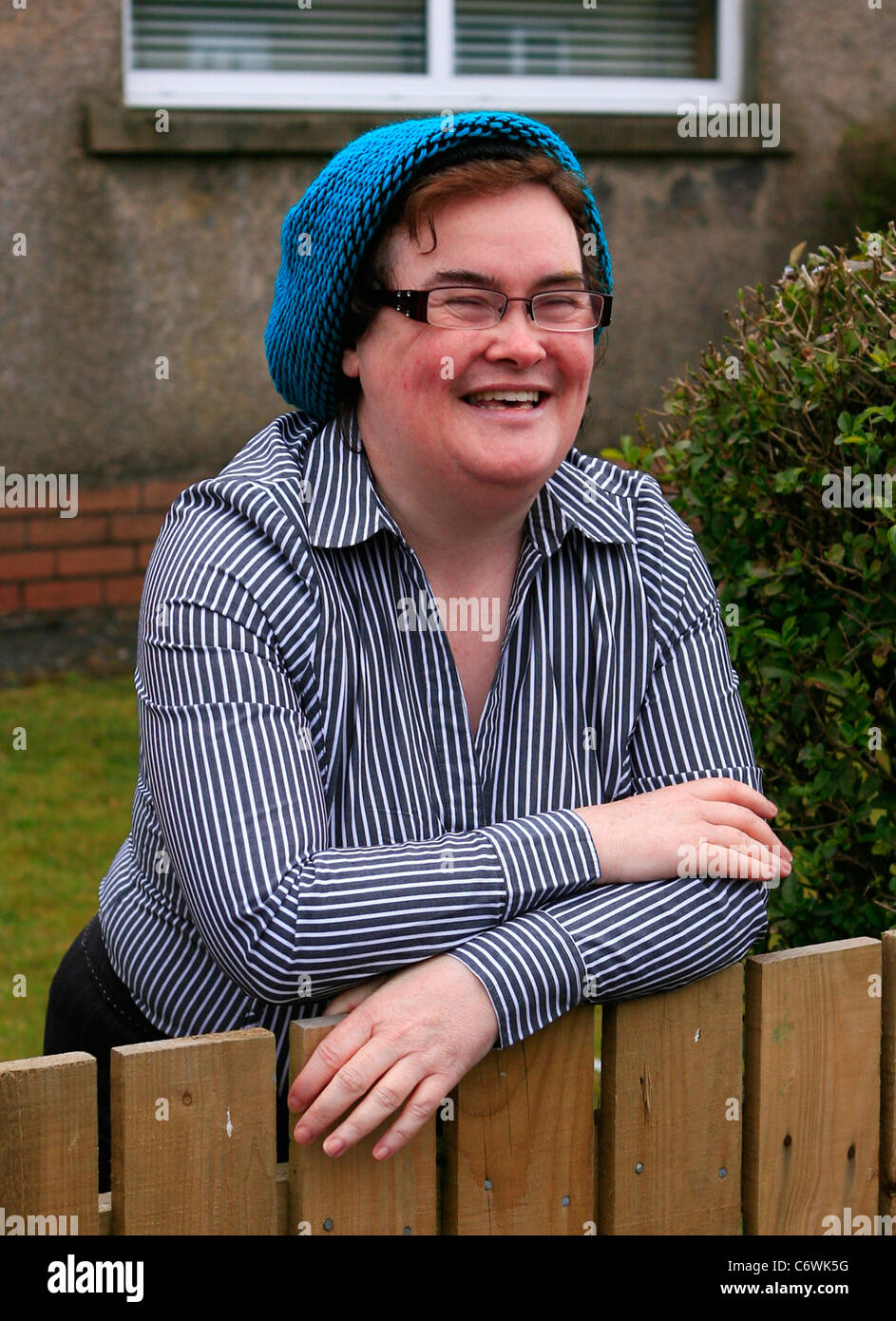 Susan Boyle in high spirits while happily chatting to photographers outside her house, wearing a blue hat and striped shirt. Stock Photo