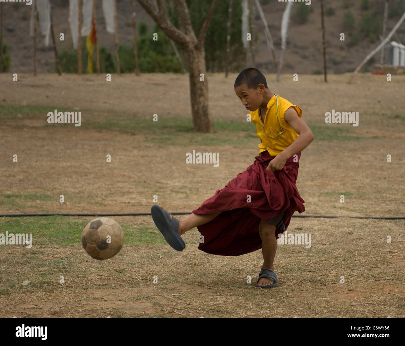 An apprentice monk in Bhutan spends his break like schoolboys everywhere in the world playing football with his mates. Stock Photo