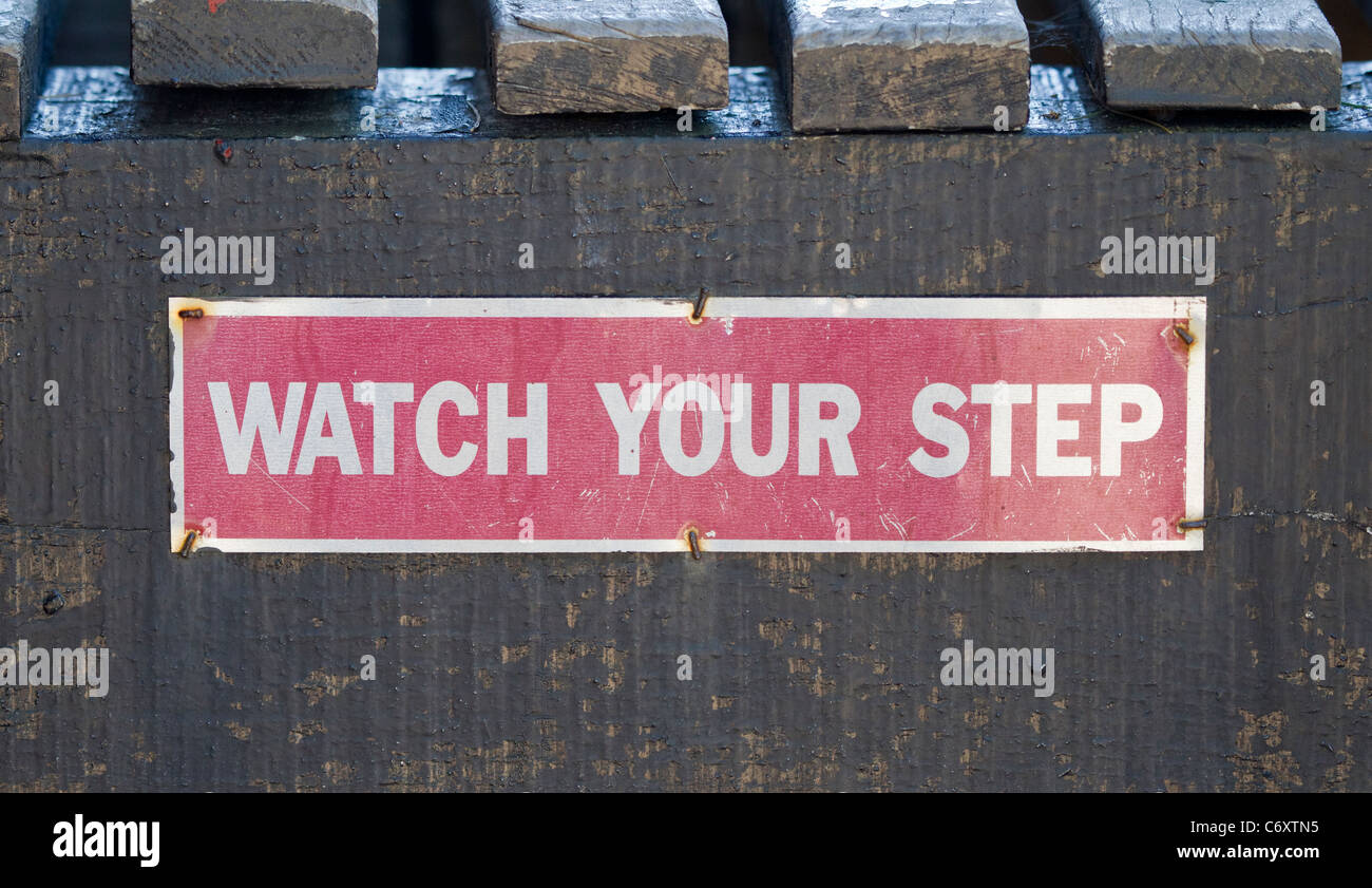 A red and white Watch Your Step sign on the top of some wooden steps. Stock Photo