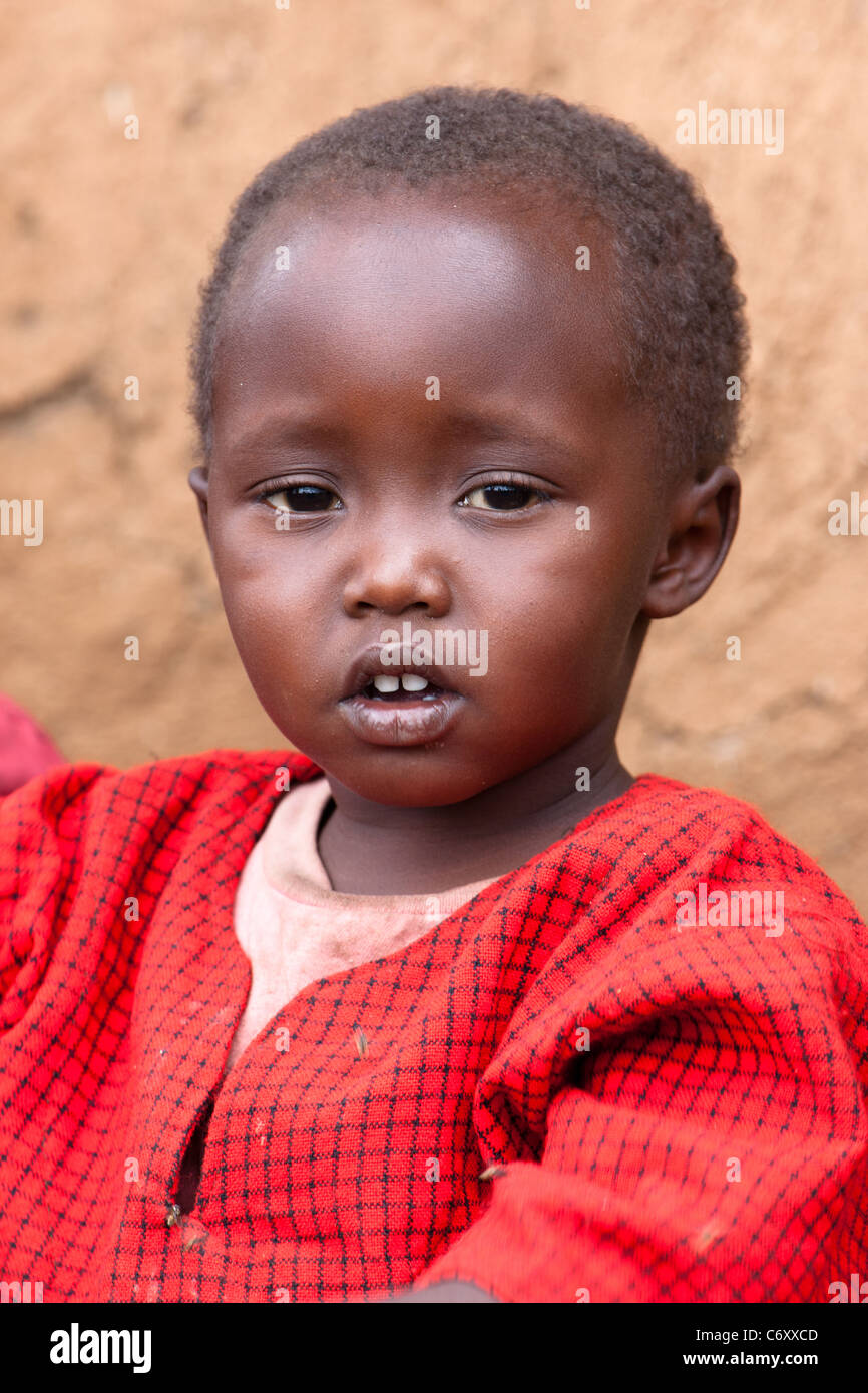 Young Maasai boy sitting in front of mud hut Stock Photo