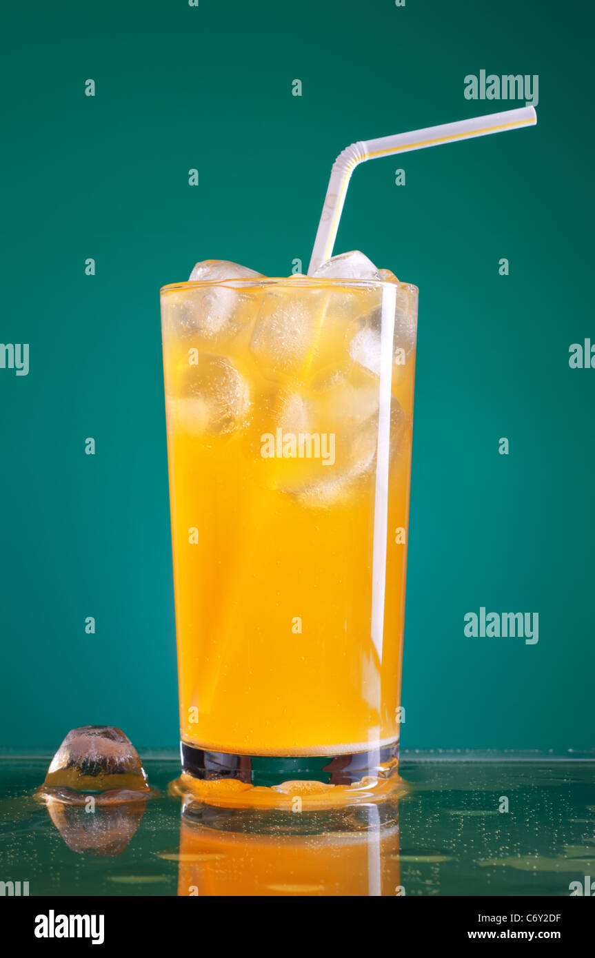 glass of orange soda with ice and straw over blue background Stock