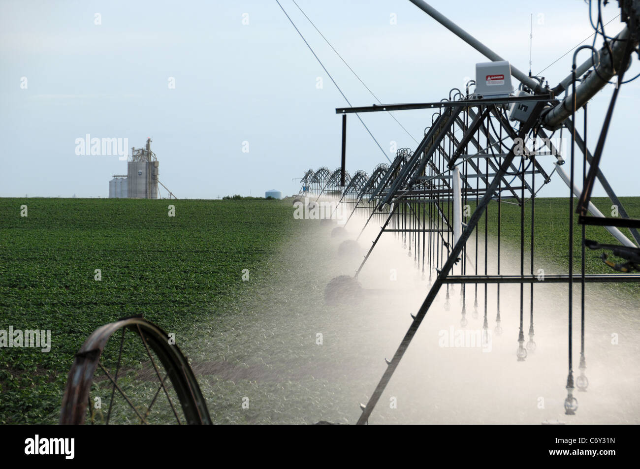 Commercial farm irrigation sprayer spraying crop with water. Grain elevator in background. Stock Photo