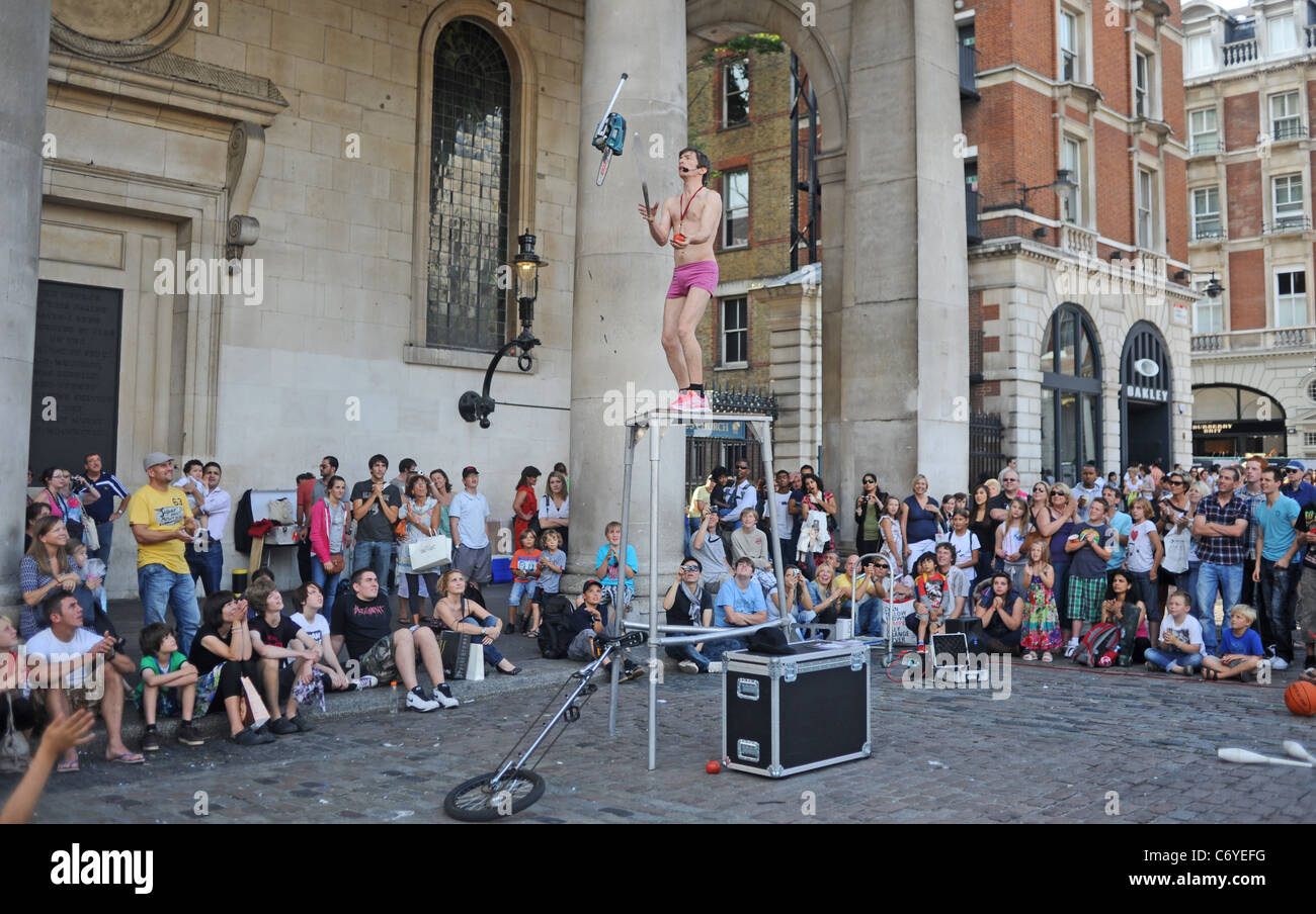 Busker male performer juggling with a chain saw in Covent Garden London UK Stock Photo