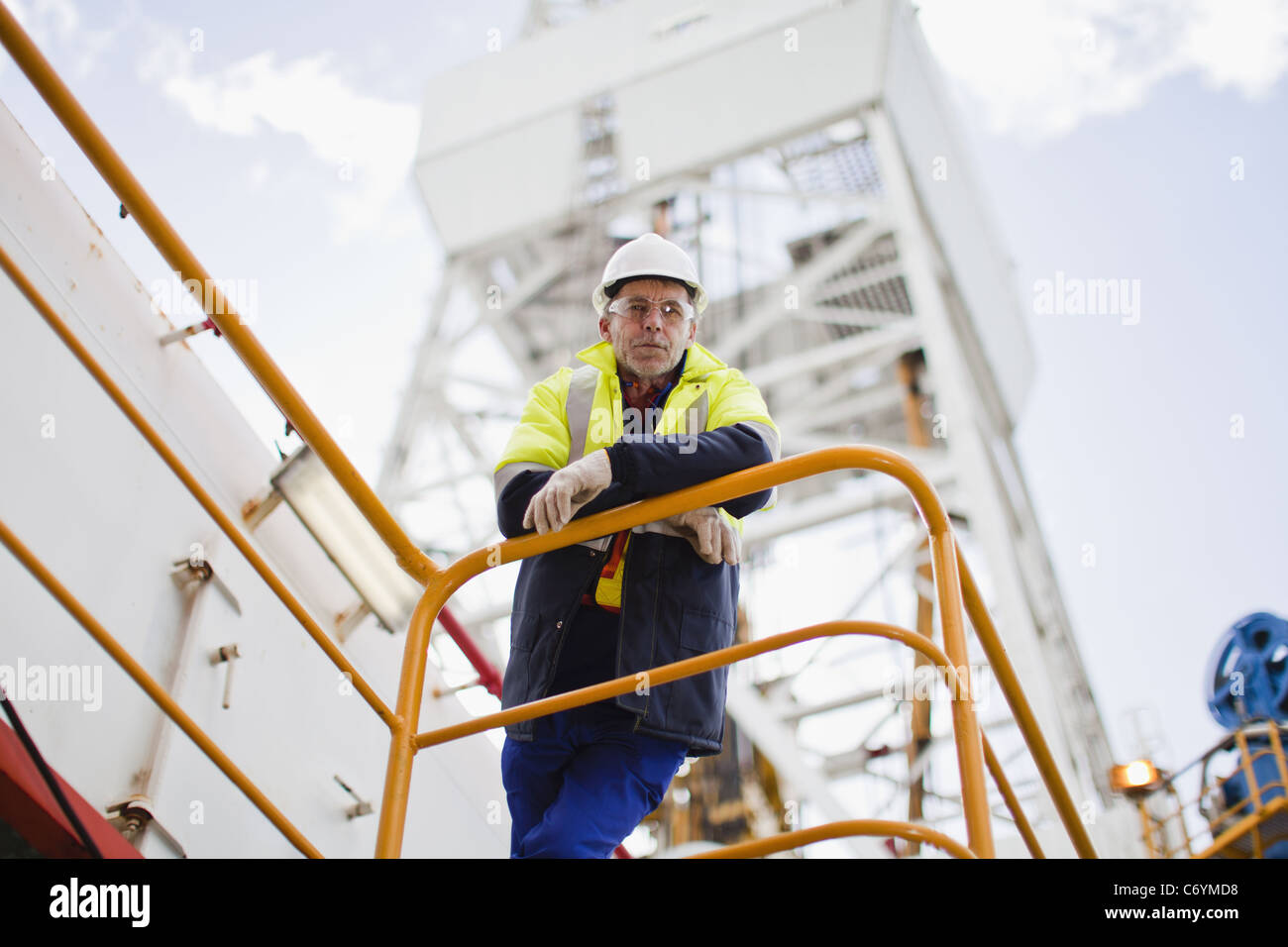 Worker leaning on railing of oil rig Stock Photo