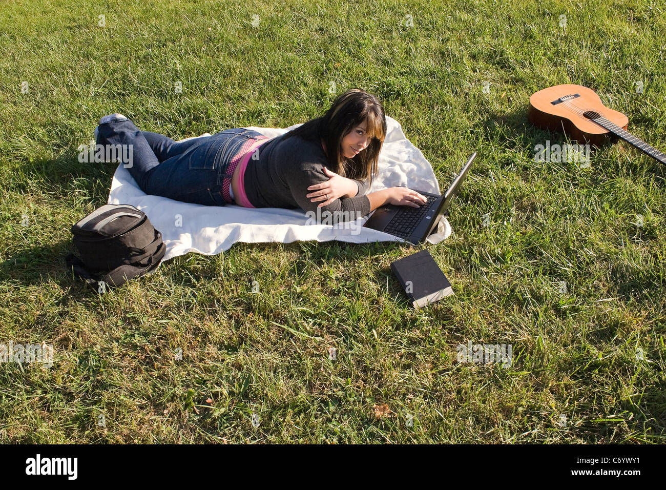 A young student using her laptop computer while laying in the grass on a nice day. Stock Photo