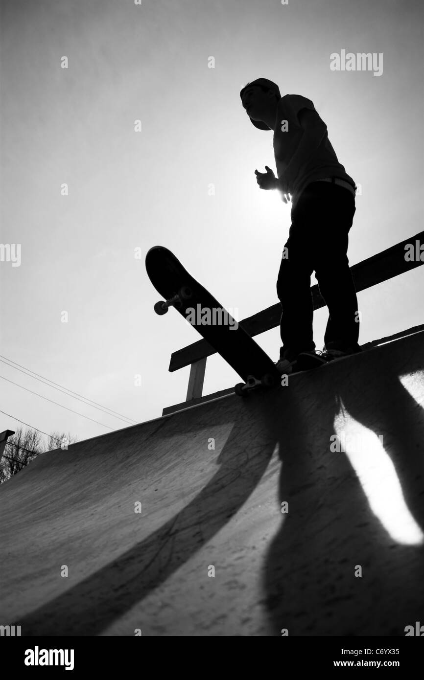Silhouette of a young teenage skateboarder at the top of the half pipe ramp at the skate park. Stock Photo