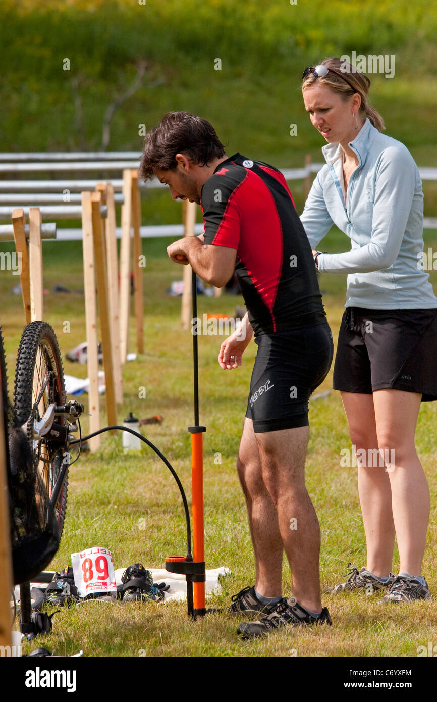 Male mountain bike racer repairs flat tire during off-road triathlon race event Stock Photo