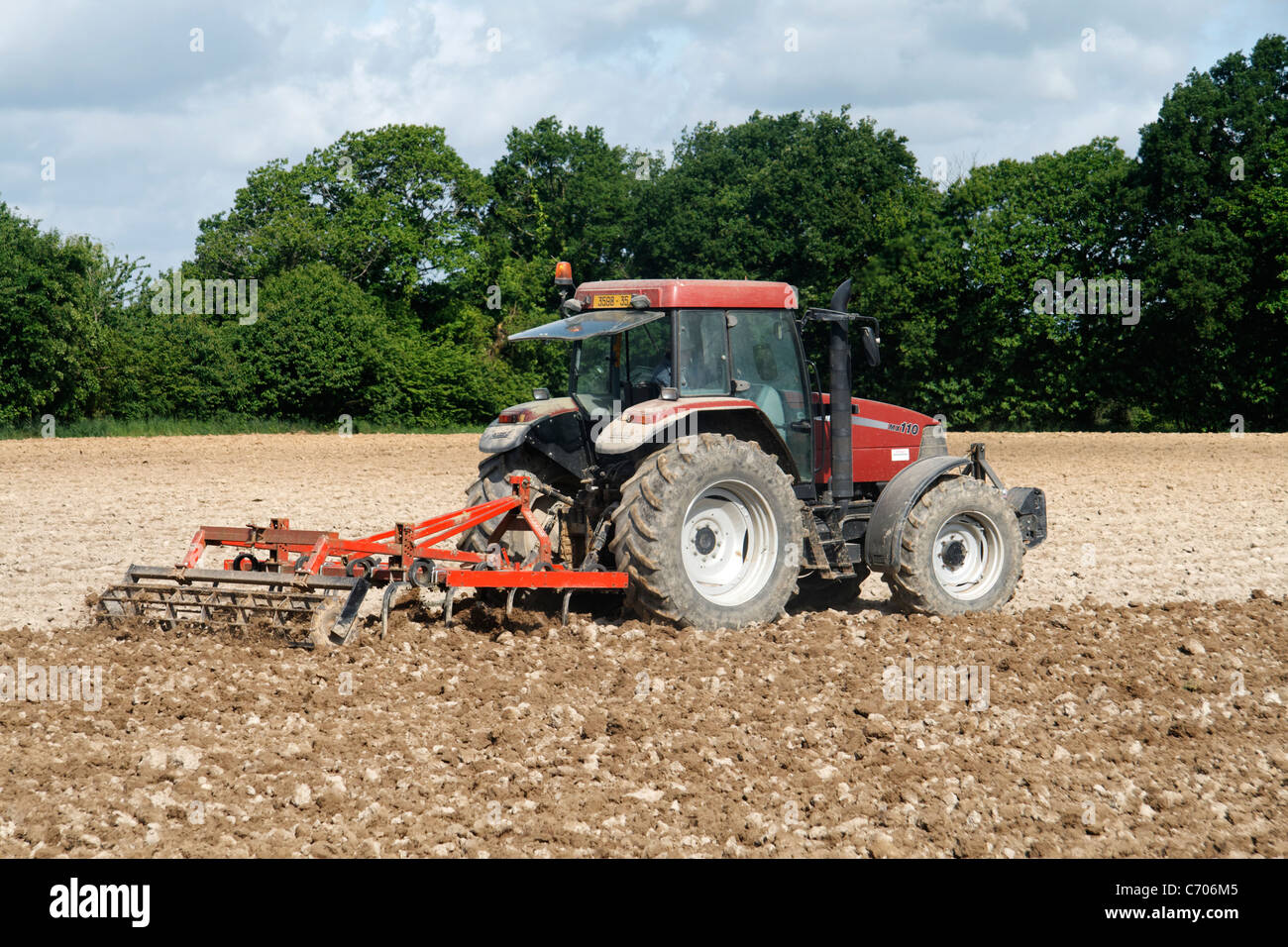 Tractor and sprung tyne cultivator harrowing ploughed field to prepare seedbed. Stock Photo