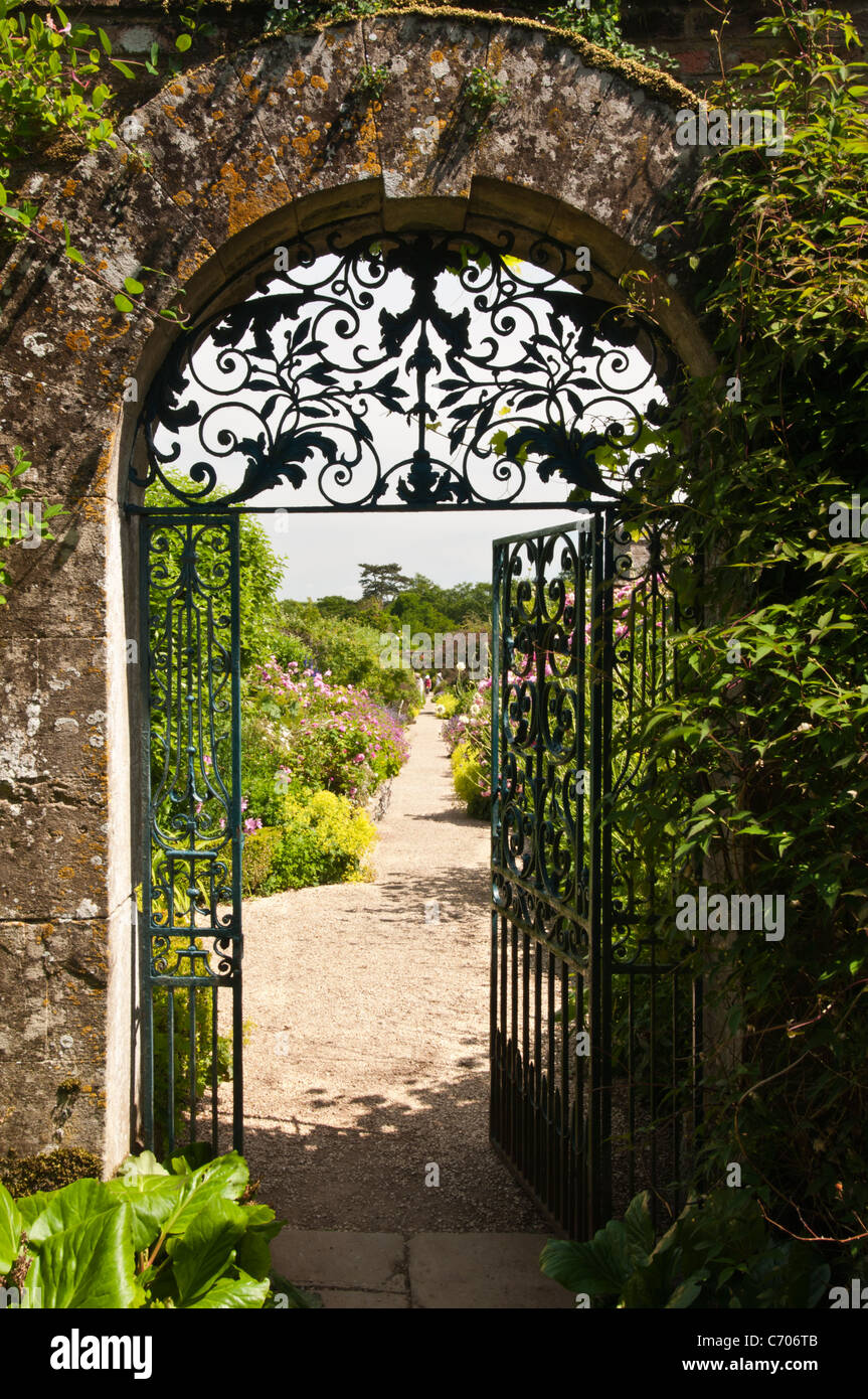 An ornate wrought-iron gate set in a Cotswold stone arch opens into