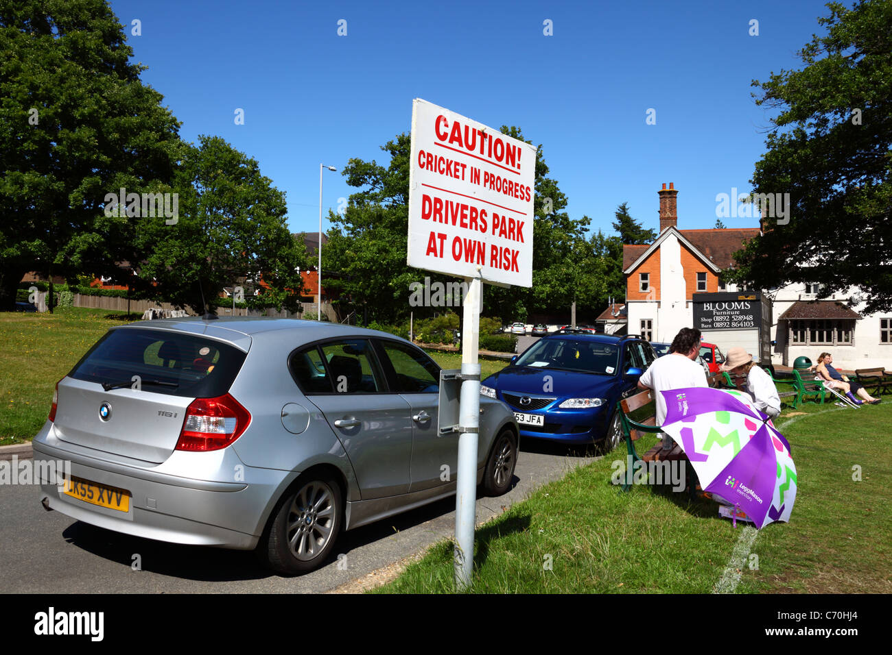 New BMW next to sign warning drivers they park by the cricket ground at their own risk while a match is in progress, Southborough Common, Kent, UK Stock Photo