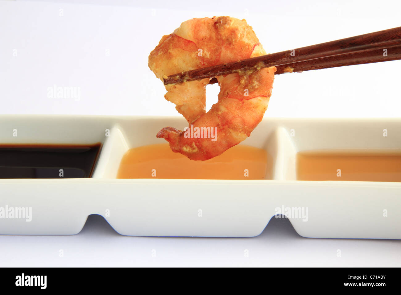chopstick holding a prawn and dipping sauces Stock Photo