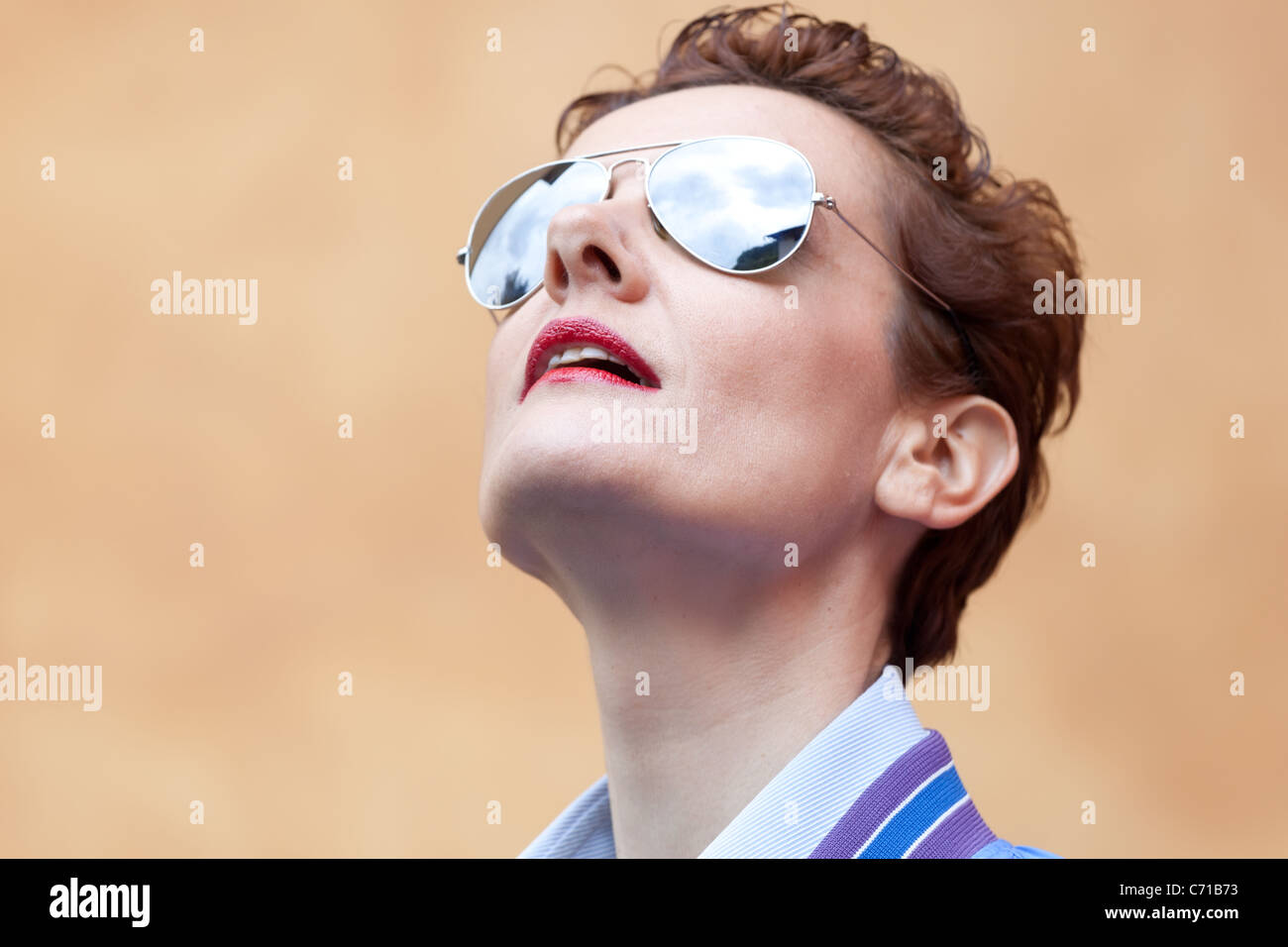 High-res headshot of modern mature woman with sunglasses looking up with curiosity. Focus on red lips Stock Photo