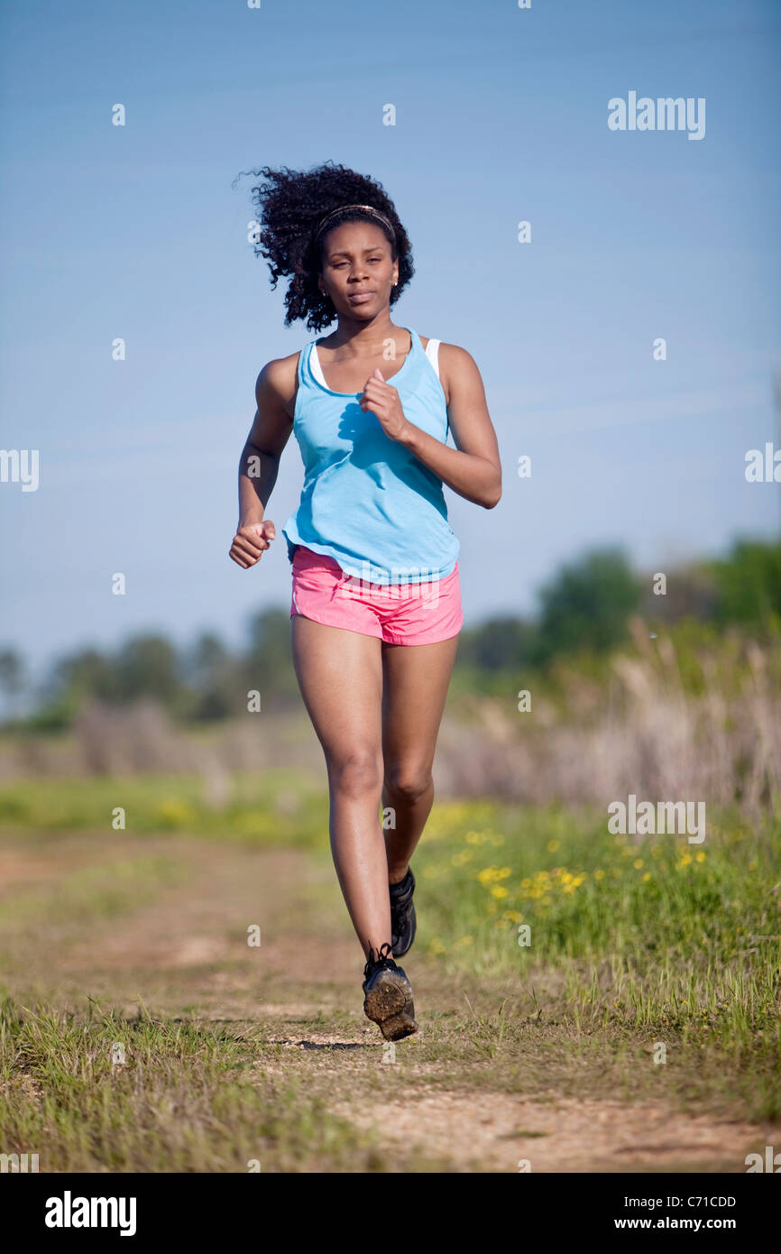 A woman runs on a dirt road through a field of wild flowers. Stock Photo