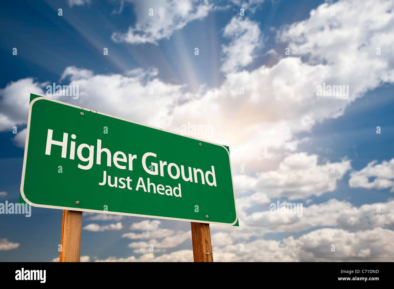Higher Ground Green Road Sign Against Dramatic Sky, Clouds and Sunburst. Stock Photo