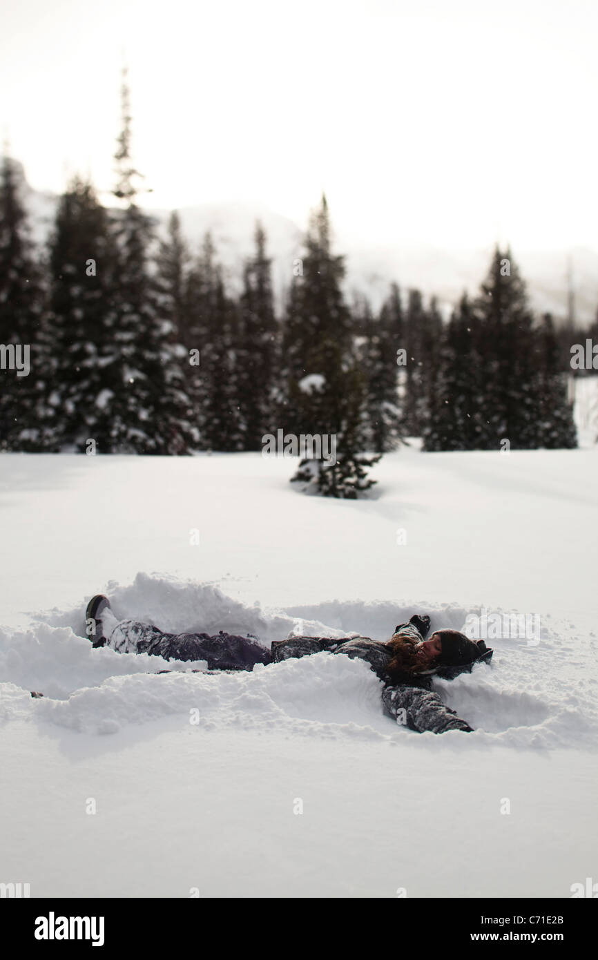 A beautiful women smiles while making a snow angel in a pristine field at sunset in Wyoming. Stock Photo