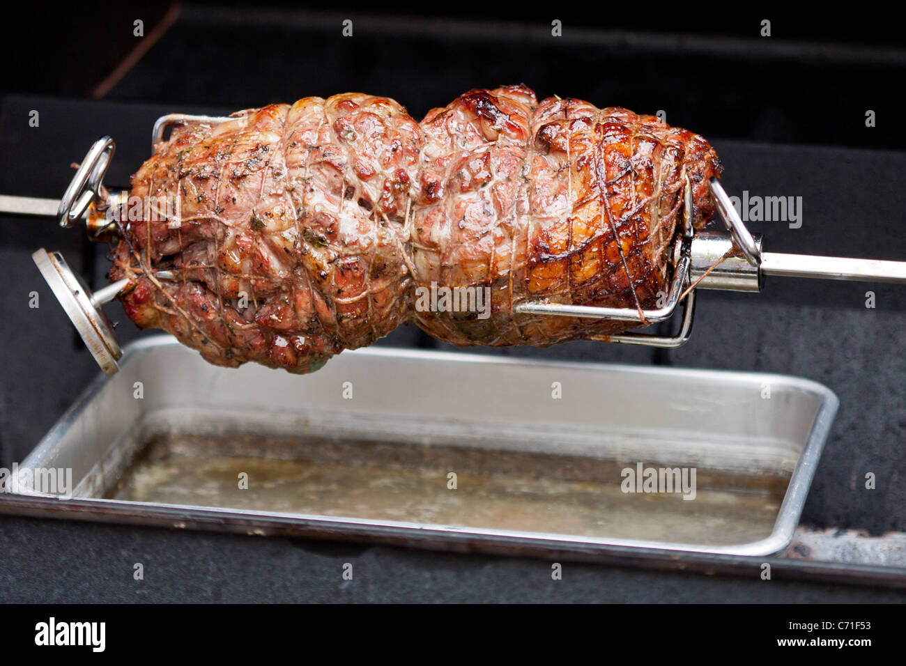 Lamb on the Spit. A pair of lamb shoulder roasts rotate on a BBQ spit. Stock Photo