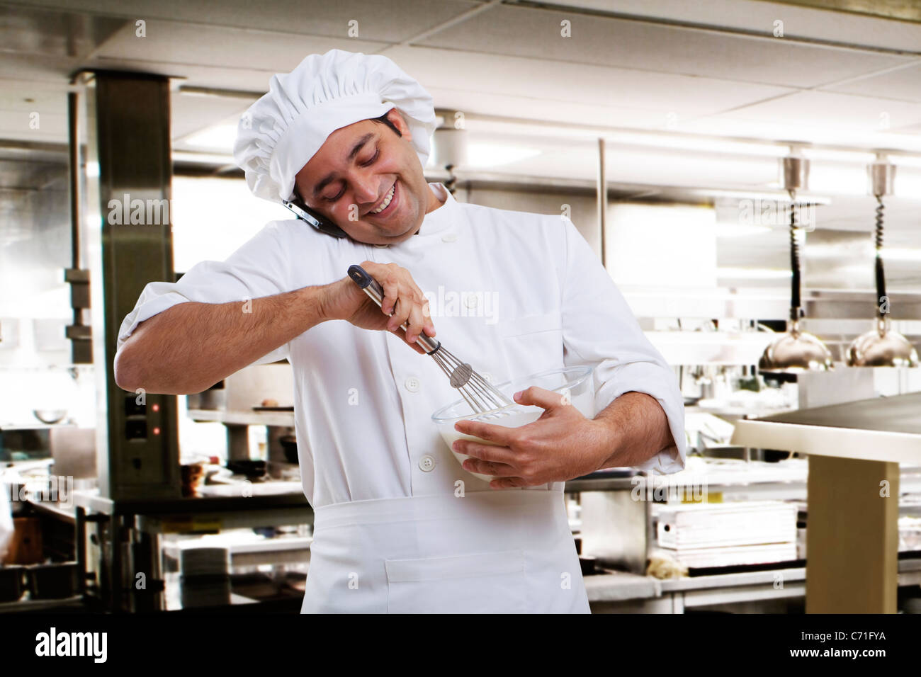 Chef talking on a mobile phone while beating dough Stock Photo