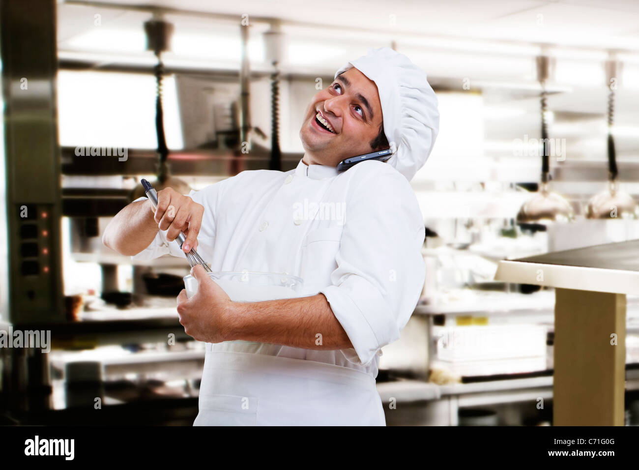 Chef talking on a mobile phone while beating dough Stock Photo