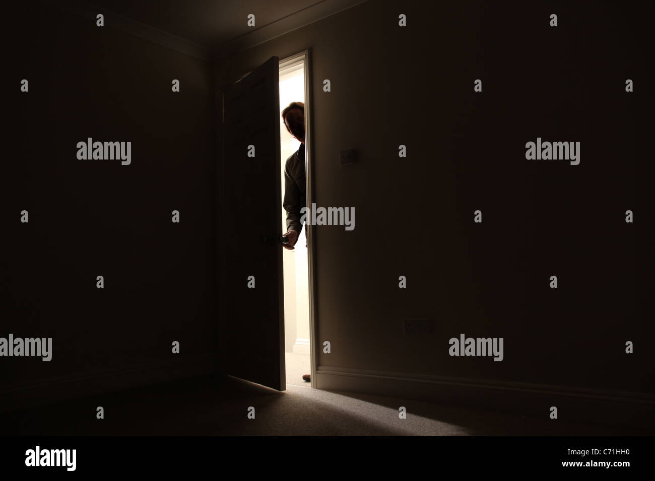 Silhouette of a male standing outside a dark room looking in. Stock Photo