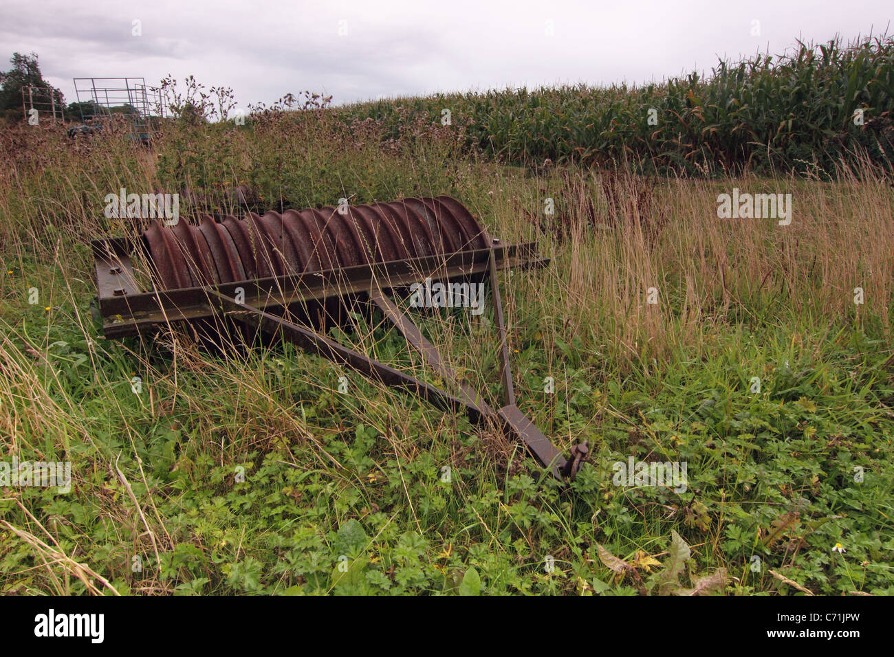 Old Overgrown farm machinery lying derelict in a field Stock Photo