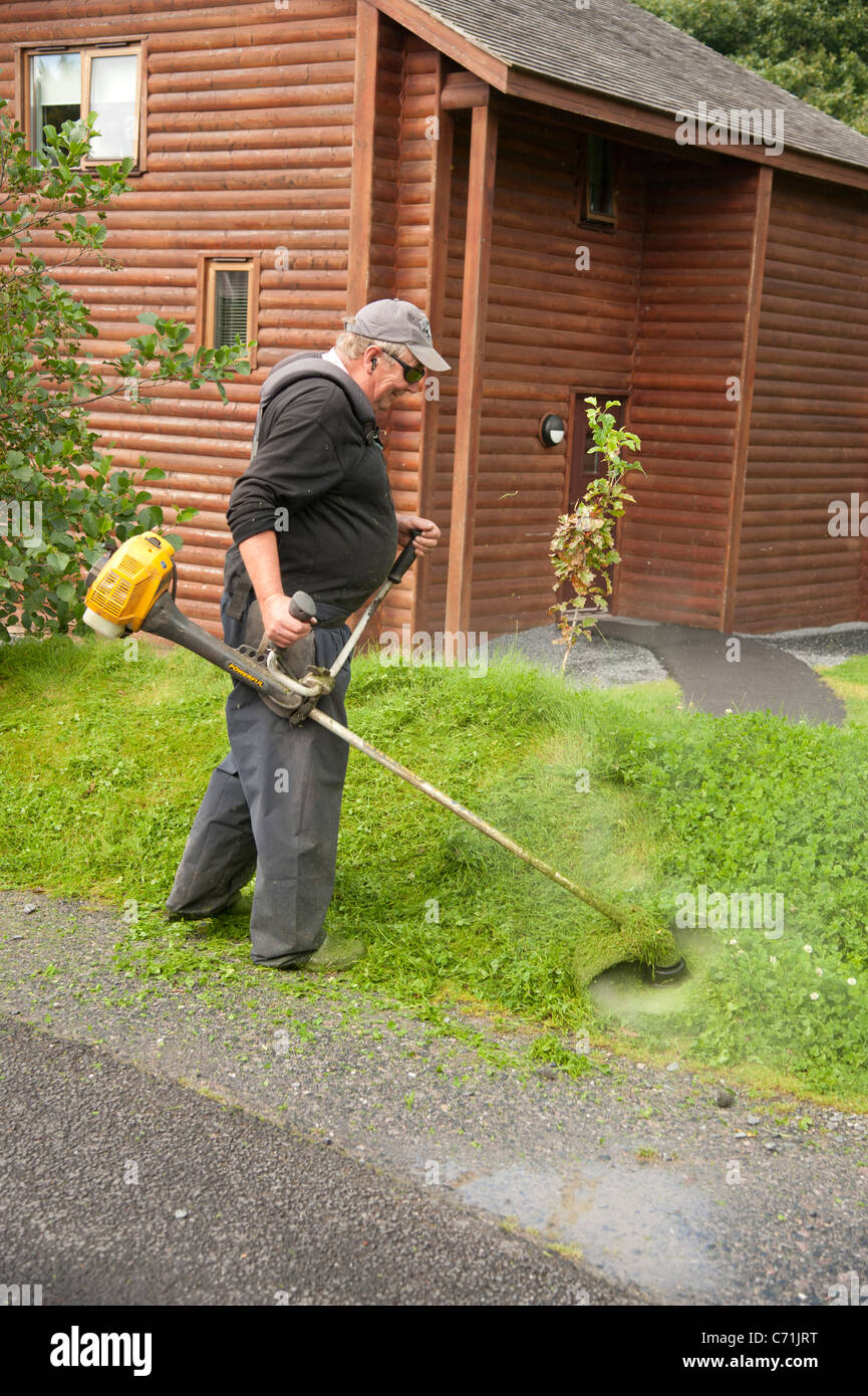 A workman cutting grass with a petrol powered strimmer at Bluestone National Park resort, pembrokeshire west wales uk Stock Photo