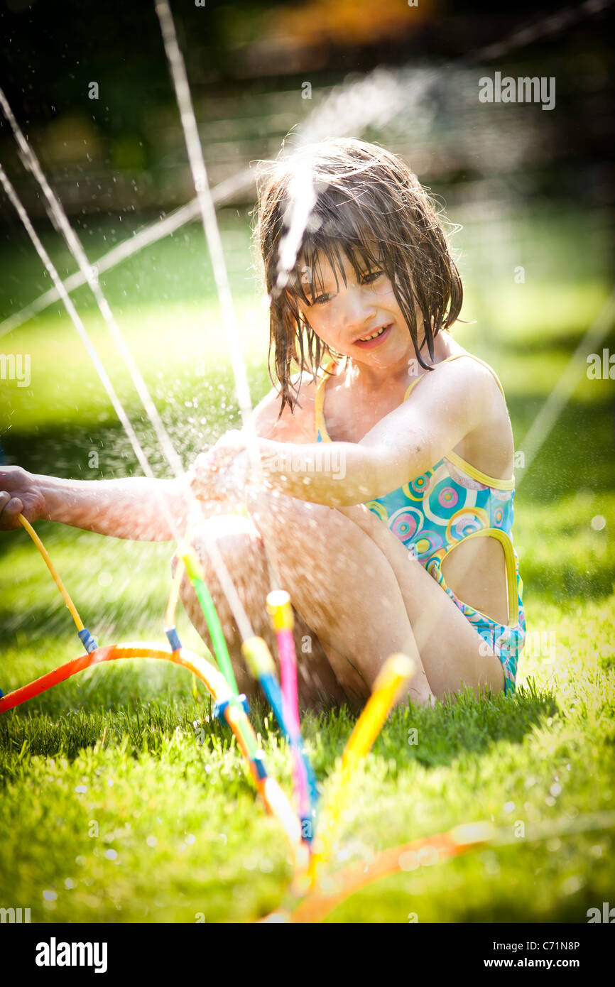 A fiveyearold girl plays in her bathing suit in a sprinkler Stock