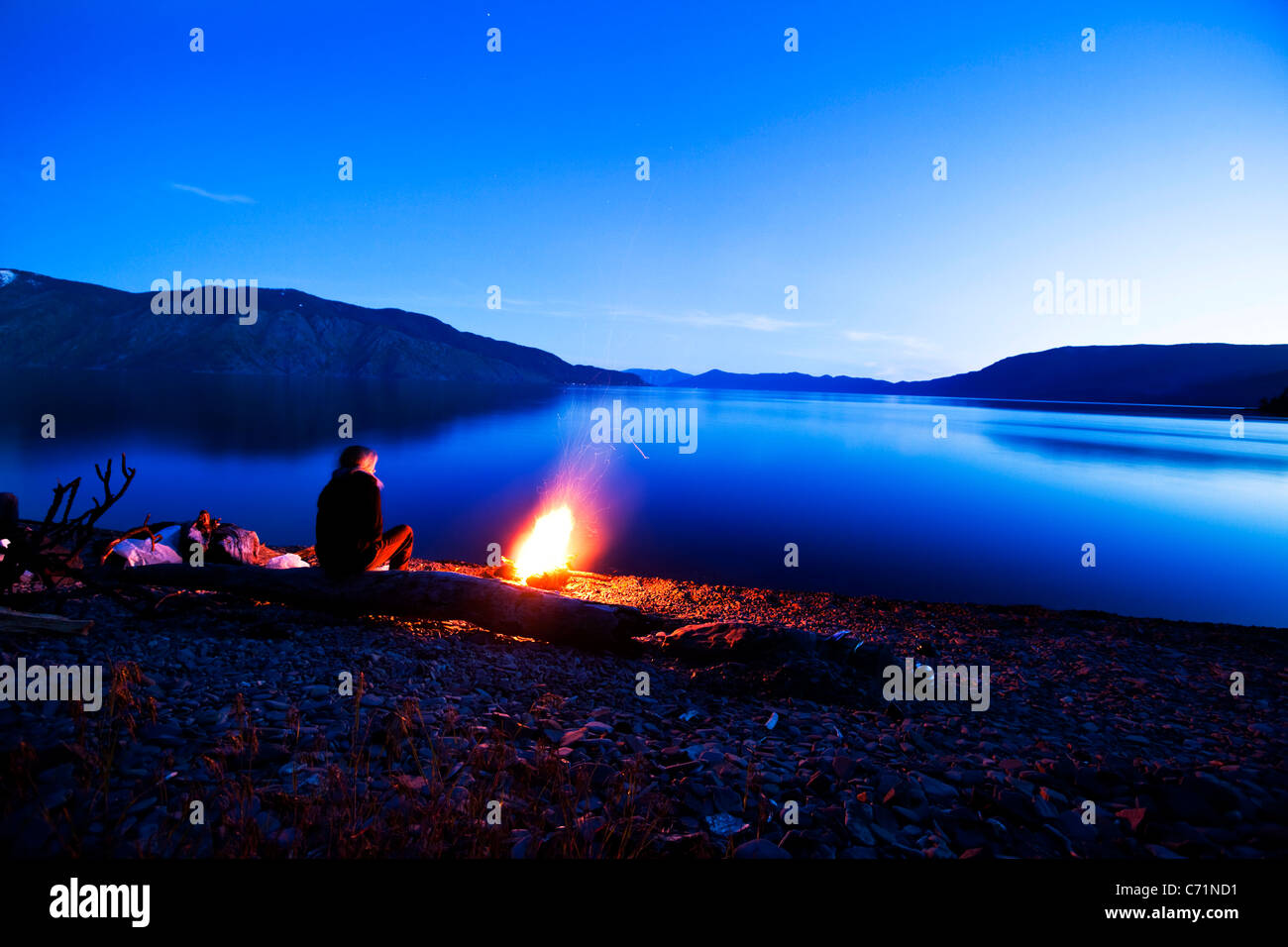 A woman sits next to a beautiful campfire at sunset in Idaho. Stock Photo