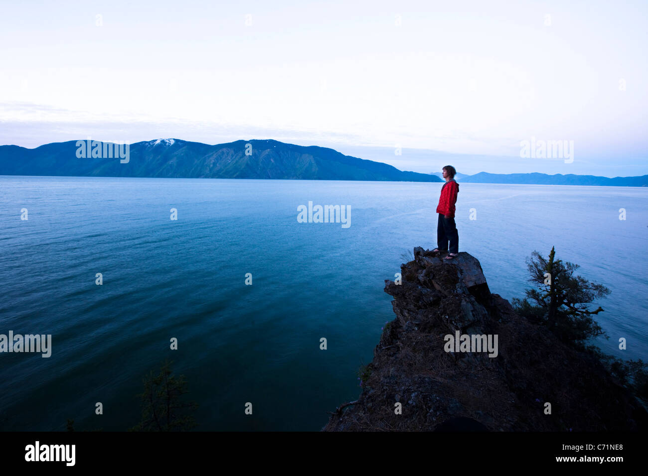 A handsome man peacefully stands on the edge of a cliff watching the sun rise over the lake in Idaho. Stock Photo