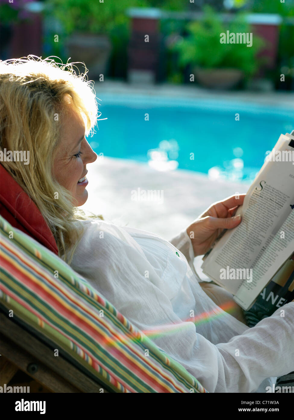 Mid age women relaxing and reading book by pool Stock Photo - Alamy