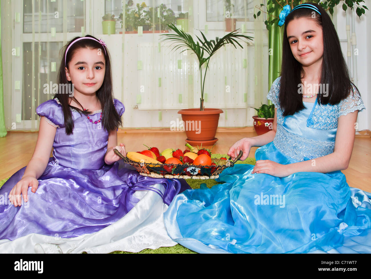 Two girls with a fruits basket in living room Stock Photo