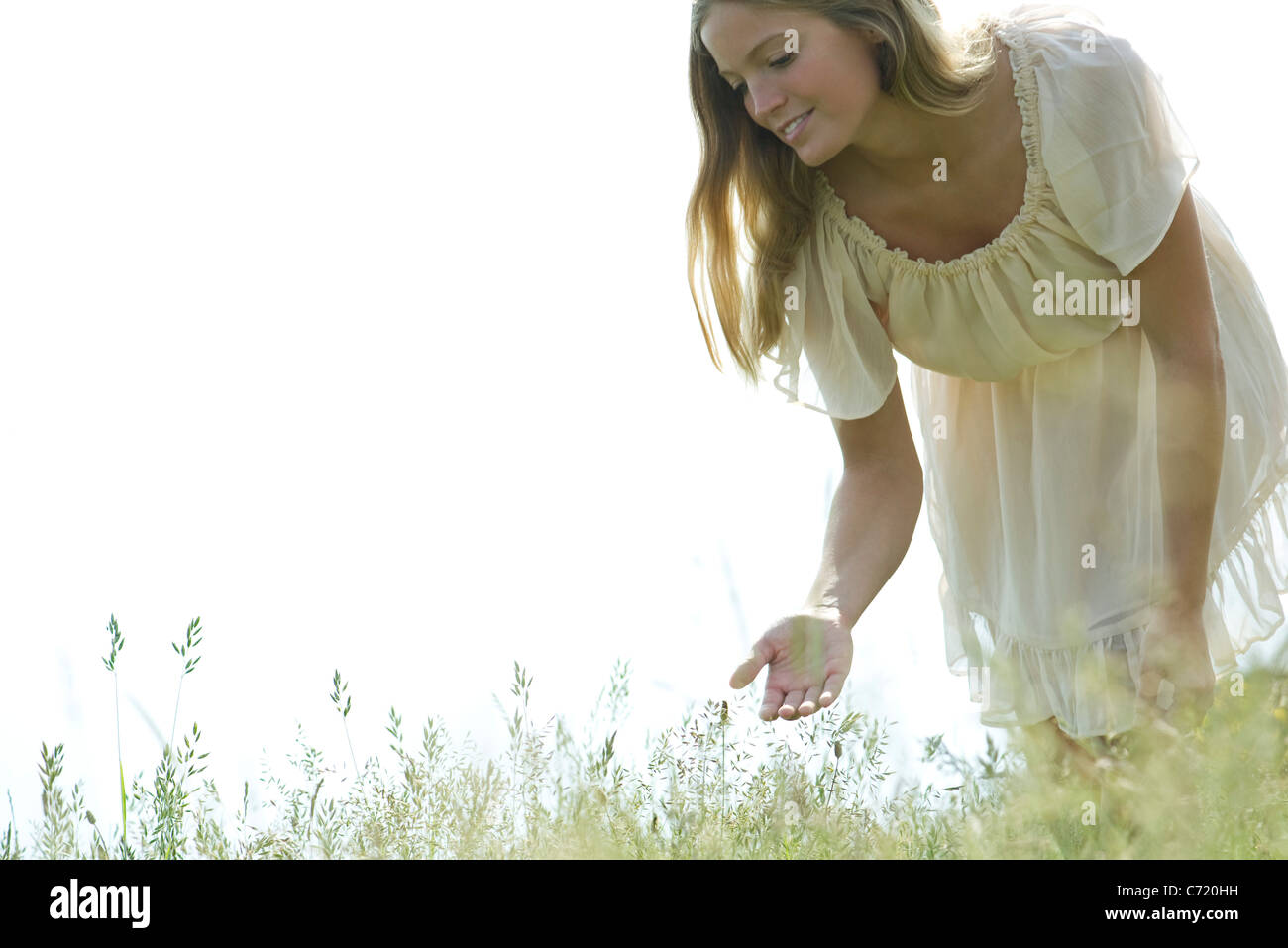 Young woman bending over to touch tall grass Stock Photo