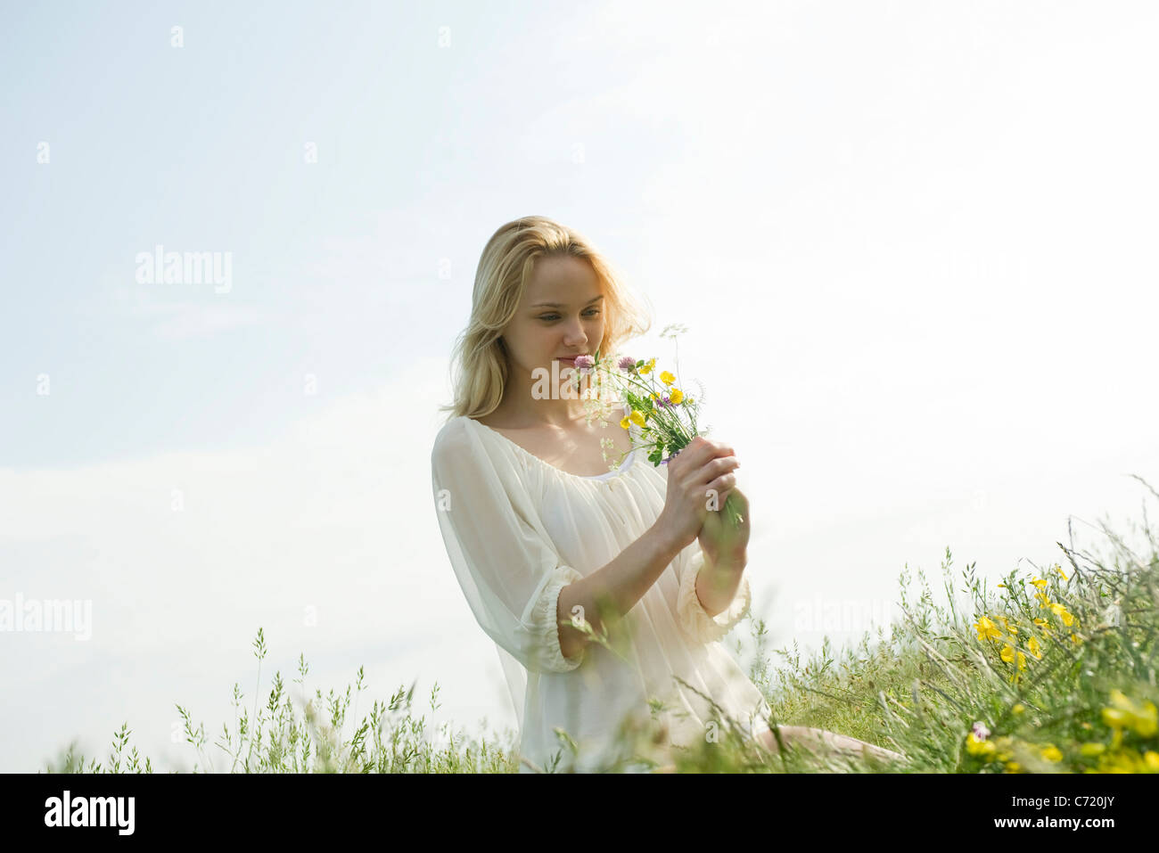 Young woman sitting in field of wildflowers, smelling bouquet Stock Photo