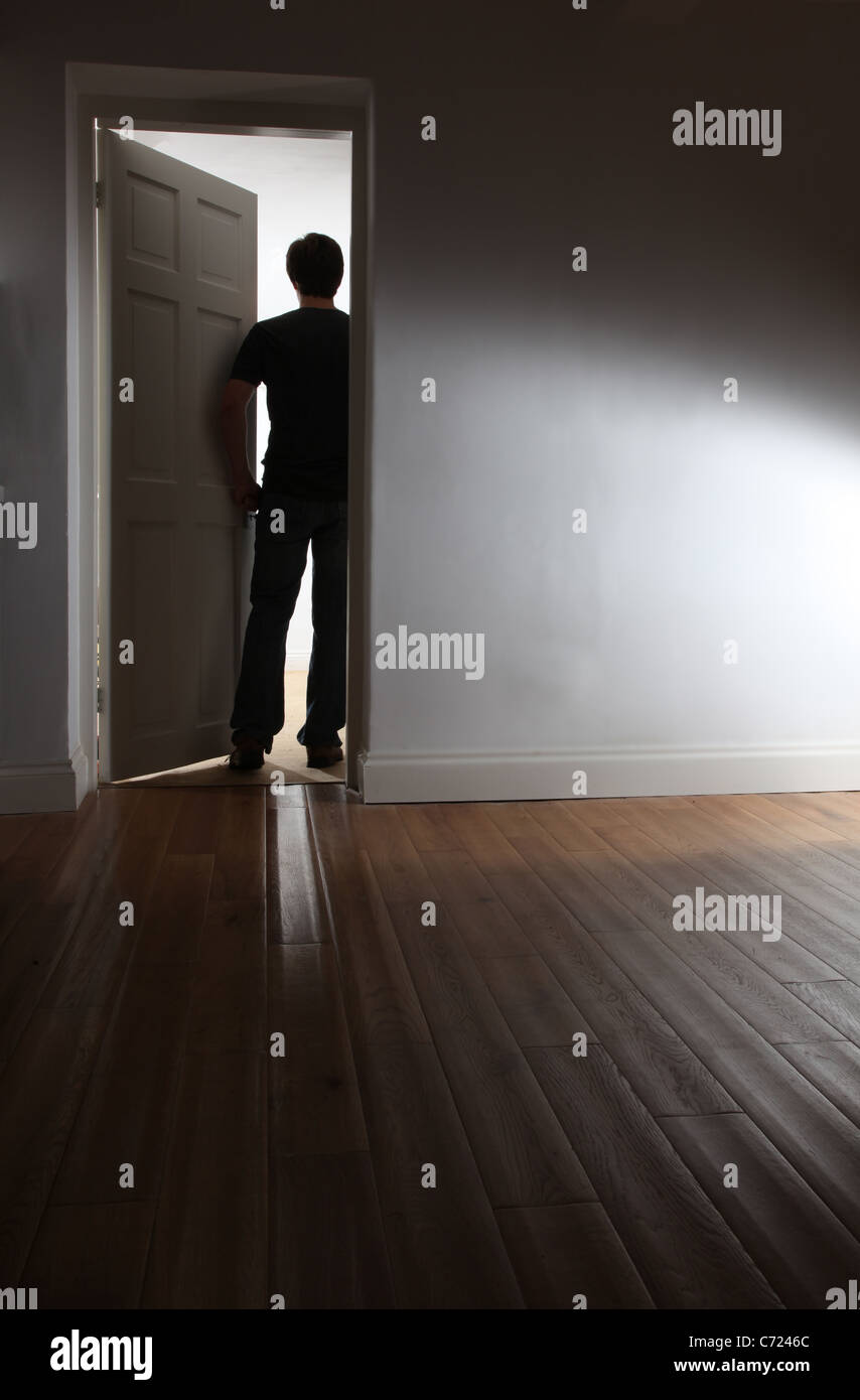 Back view of a shadowy male walking out of a dark room. Stock Photo