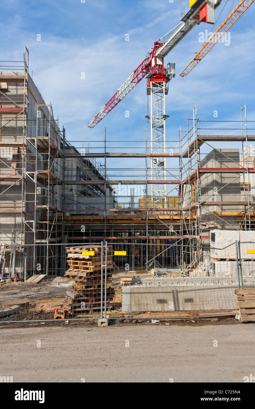 Large construction site with scaffolding building, yellow tower crane and clear blue sky. Stock Photo
